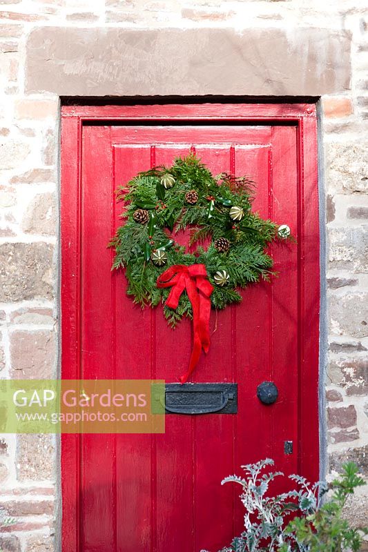 Christmas wreath with pine cones berries and dried fruit and red bow on red door