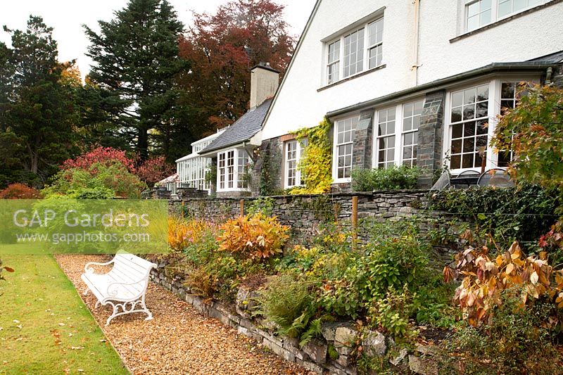 A herbaceous border with autumnal plant foliage in front of the Arts and Crafts style house at High Moss, Portinscale, Cumbria, UK