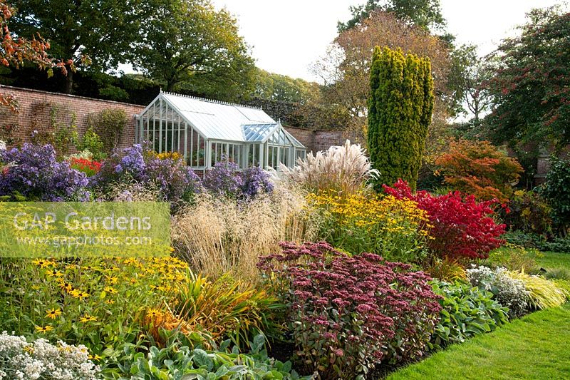 A glasshouse and herbaceous beds of Rudbeckia, Sedum, Asters, and Pennisetum in the walled garden at Holehird Gardens, Windermere, Cumbria, UK