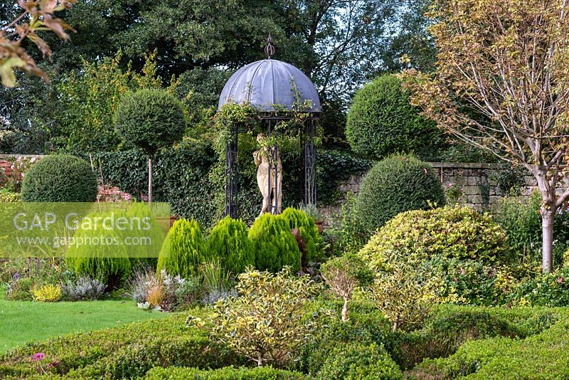 A classical style gazebo surrounded by tall privet standards and dwarf golden green conifers, Thuja orientalis 'Aurea Nana'.