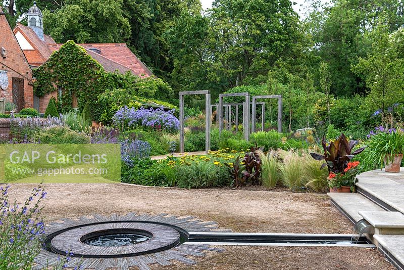 View into the contemporary lower garden, over a rill of prairie style borders planted and a path straddled by an oak pergola.