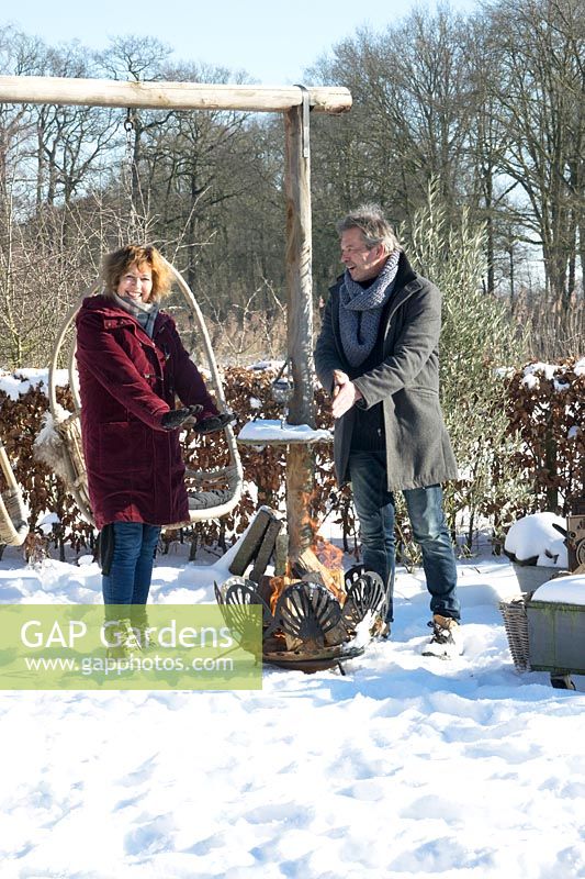 Man and wife Martijn and Liesbeth, warming their hands near the fire basket in the snow.