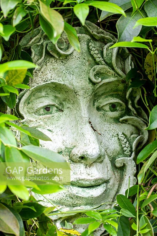 Ceramic face surrounded by foliage