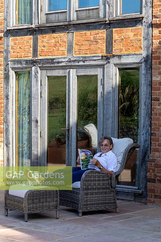Woman sitting on patio reading with house behind