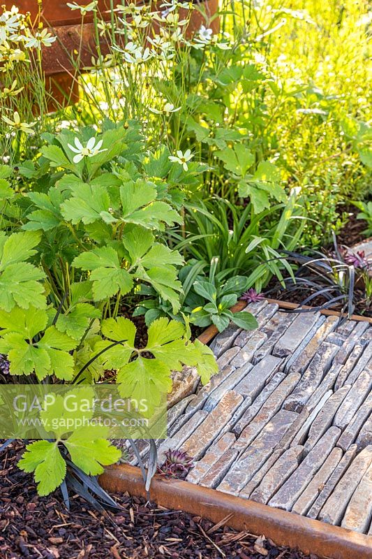 Stepping stone made from corten steel filled with pieces of natural stone next to perennial plants. Through Your Eyes Garden.