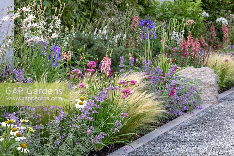 Colourful, nectar-rich, mixed summer border next to contemporary stone edged grey gravel path. The Viking Cruises Lagom Garden - Hampton Counrt Flower Festival, 2019.
