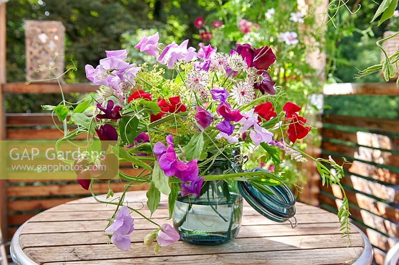 Flower arrangement of Lathyrus odoratus - Sweet Pea - and other cut flowers in a glass jar on a wooden table