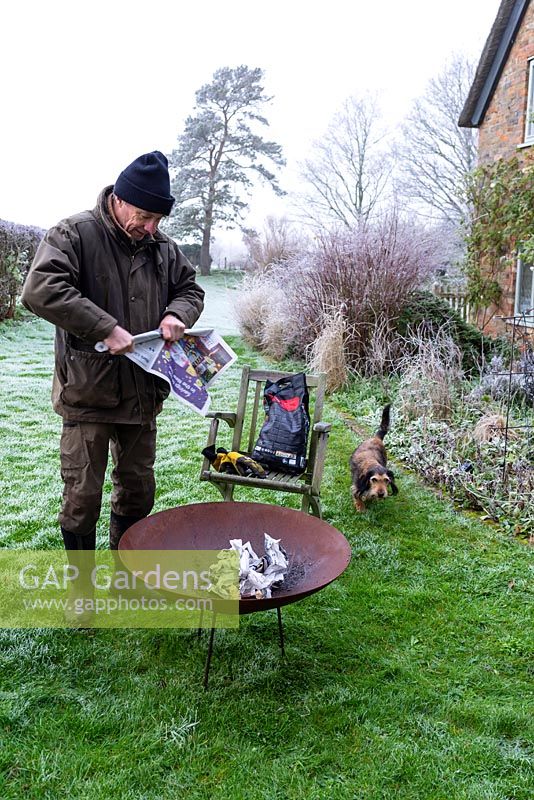 Man lighting a corten steel fire pit with rolled up newspaper on a frosty winter day. 