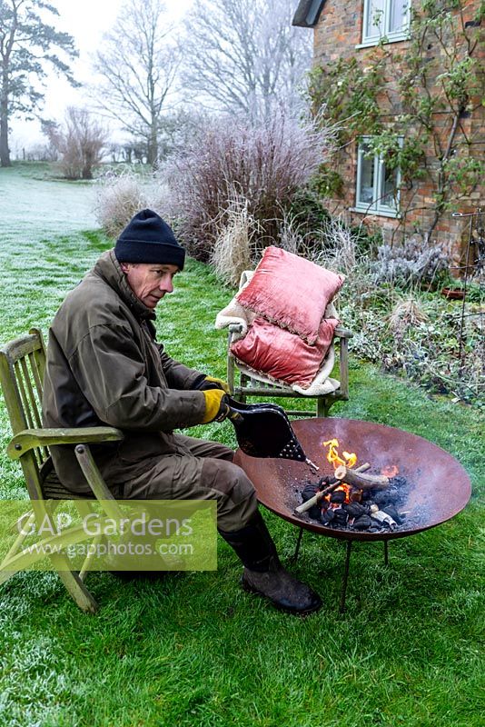 Man lighting a corten steel fire pit with bellows on a frosty winter day. 