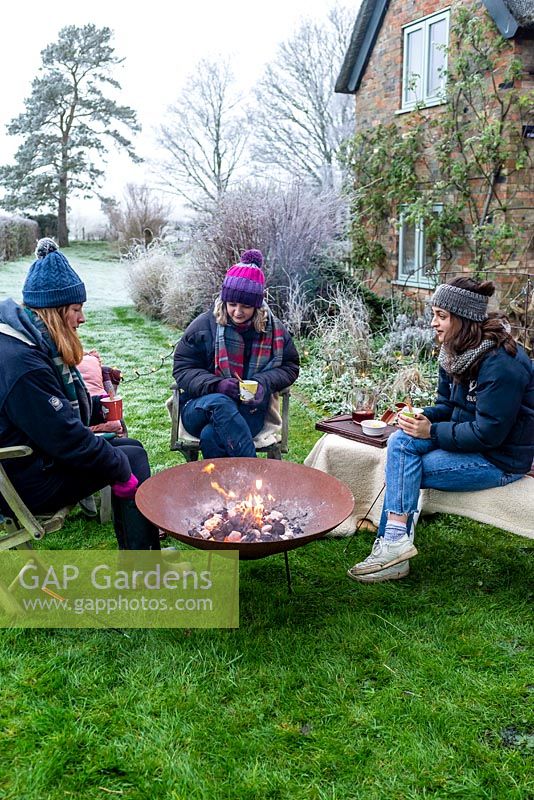 Women sitting around a fire in a corten steel fire pit, drinking mulled wine on a frosty winter day.