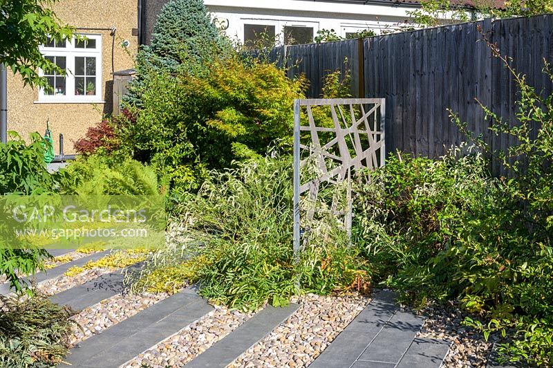 Decorative powder-coated aluminium pattern screens in shrub and perennial border in modern, North London garden by Earth Designs. 
