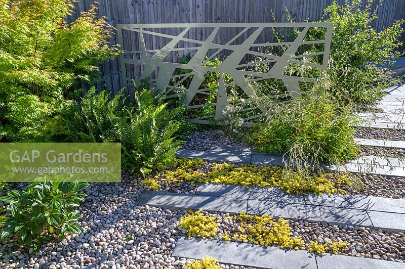 Decorative powder-coated aluminium pattern screens in shrub and perennial border in modern, North London garden by Earth Designs.