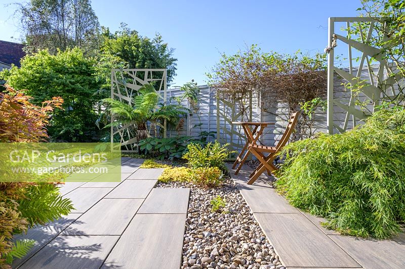 Paved sitting area with  wooden bistro table and chairs, in modern, north London garden by Earth Designs. 