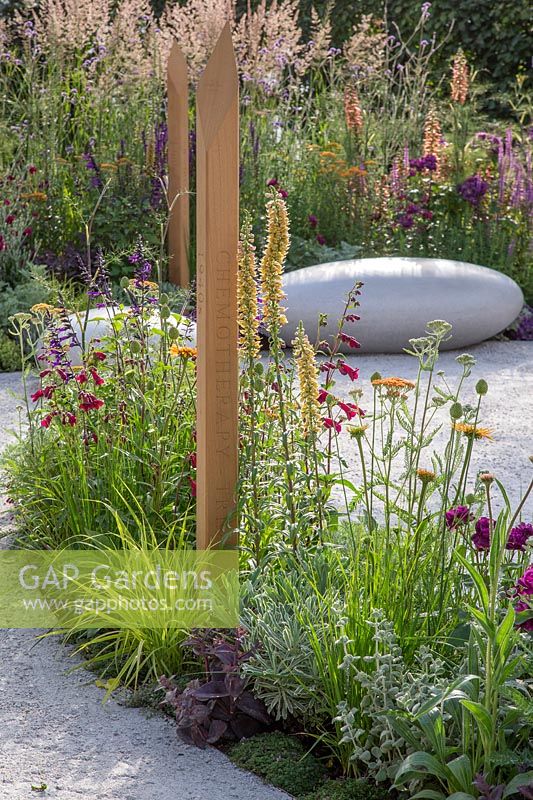 Compacted path surrounds border with colourful summer perennials leading to large smooth feature stone seating. The Cancer Research UK Pledge Pathway to Progress - Hampton Court Flower Festival, 2019.