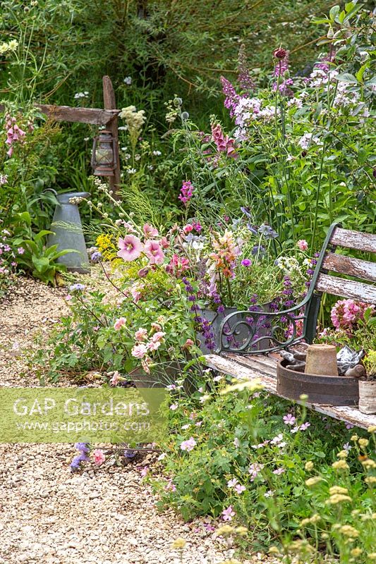 View along a crushed stone pathway through a wildlife friendly garden with wooden bench. Springwatch Garden, Hampton Court Flower Show, 2019.
