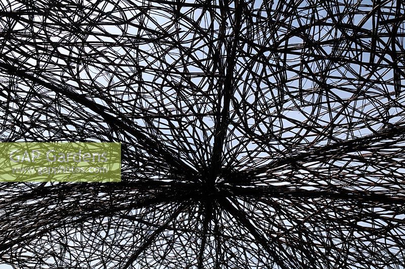 Looking up at a silhouetted willow structure forming the roof of the PMS: Outside Inside for NAPS Garden - RHS Hampton Court Palace Flower Show 2016