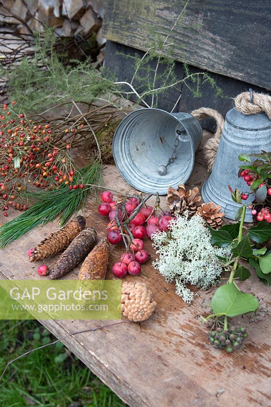 Materials for making a rustic Christmas wreath including rosehips, crab apples, pinecones and foliage hanging from two metal bells. Styling by Marieke Nolsen. 