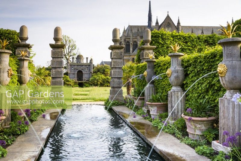 The Collector Earl's Garden at Arundel Castle, West Sussex in May. Designed by Isabel and Julian Bannermann. Green oak urns with gilded lion spouts and agaves line water representing an allegorical River Arun, leading towards Oberon's Palace. Terracotta pots are planted with agapanthus and surrounded by Alchemilla mollis and alliums.