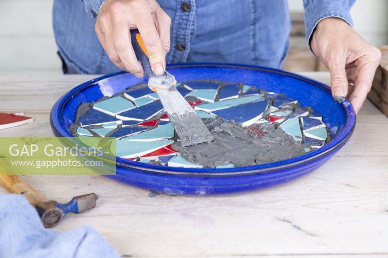 Woman using a scraper to  spread grout over the top of the mosaic
