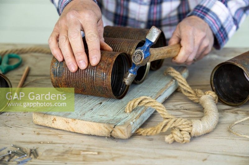 Woman using a hammer to nail tin cans to a wooden board