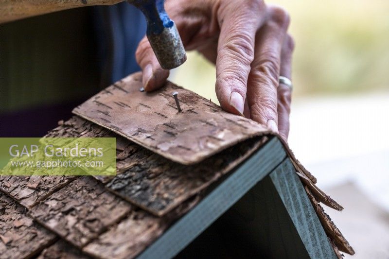 Close up of woman using a hammer to nail a wider sheet of bark over the top of the roof