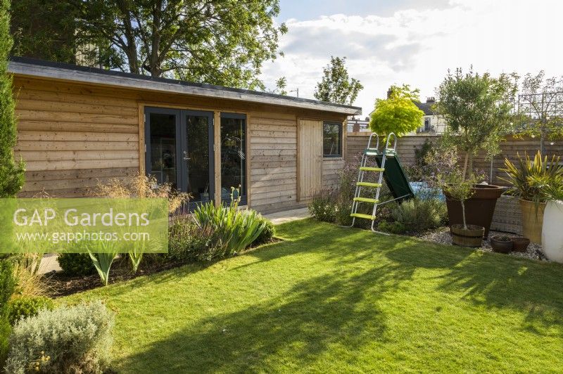Modern wooden outbuilding with lawn children's play area with colourful slide in modern family garden 