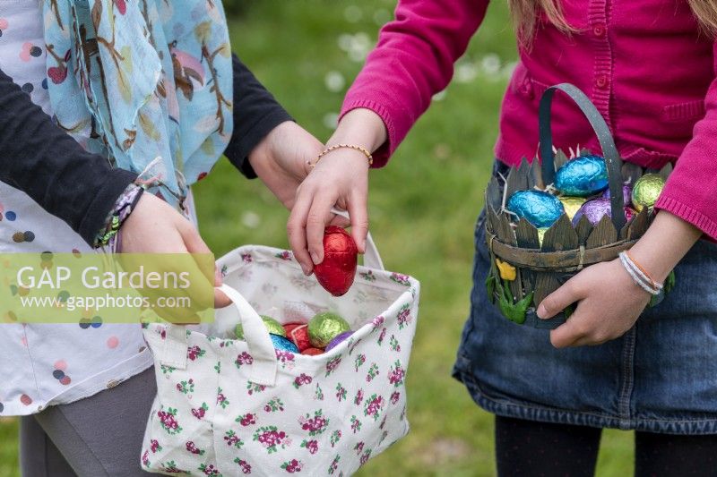 Children collecting colourful chocolate eggs in baskets at Easter