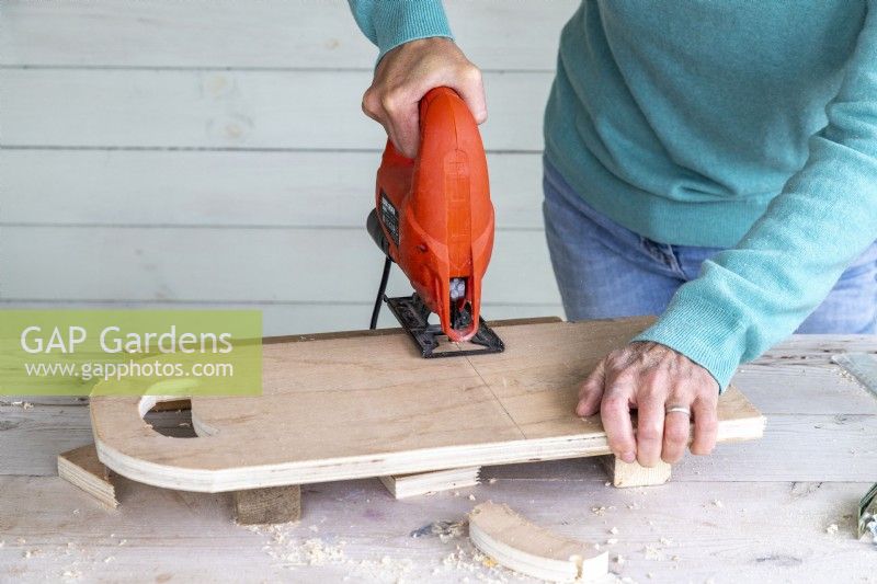 Woman using a jigsaw to cut the wooden board in two