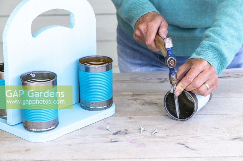 Woman using a hammer and pin punch to create a hole in the cans