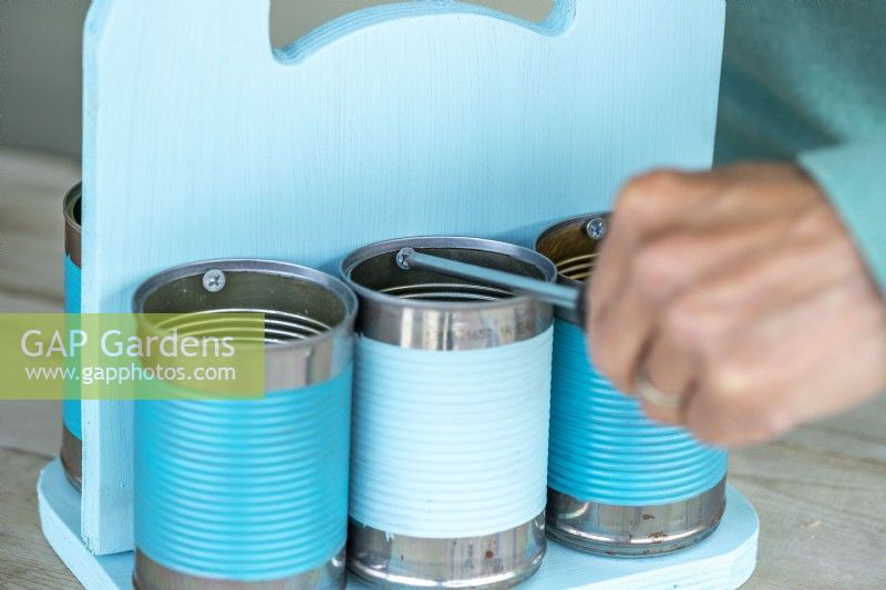 Woman using screwdriver to attach the cans to the wooden boards
