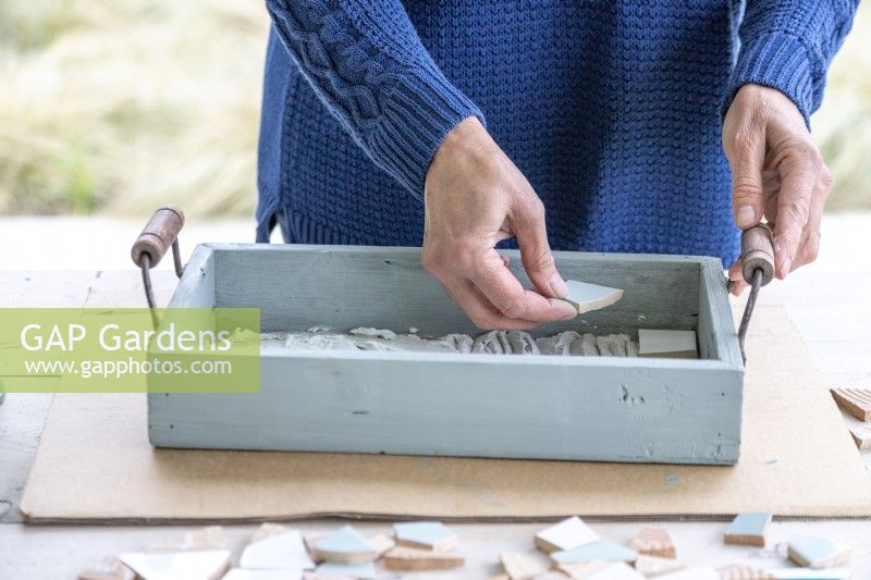 Placing a piece of tile in a tray to make a mosaic