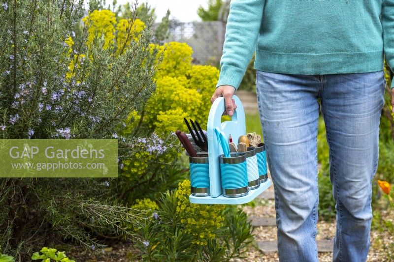 Woman carrying pastel tin can caddy containing garden tools and supplies