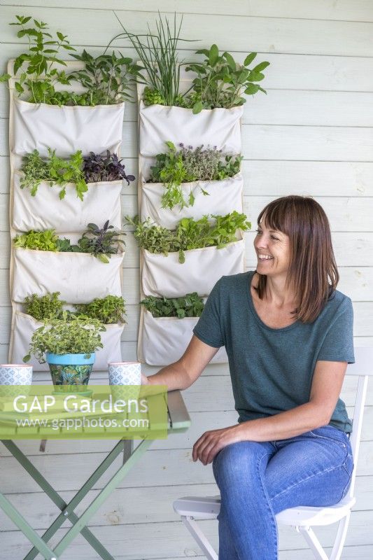 Woman sitting at a table next to hanging herb and salad garden