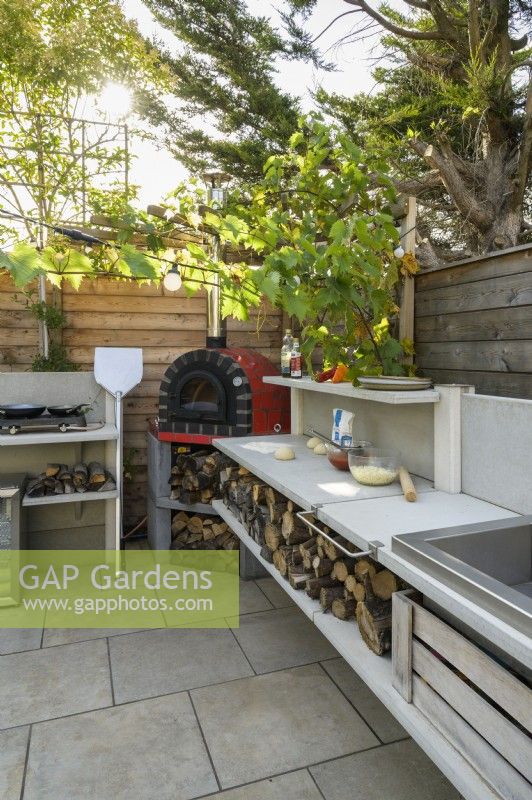 Outdoor kitchen with red pizza oven, sink hob and wood storage