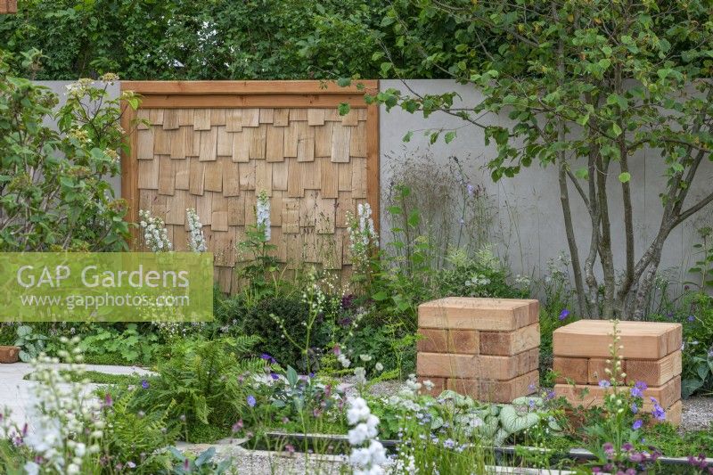 The Communication Garden. A tranquil refuge with woodland planting and a wall screen made from sweet chestnut edged in Delphinium 'Guardian White'.