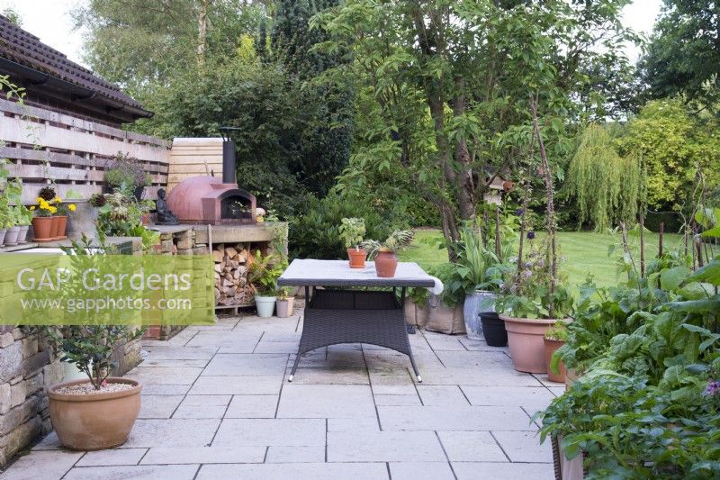 Summer outdoor kitchen with sink, oven, wood store and dining area and surrounded with containers planted with herbs and vegetables. 