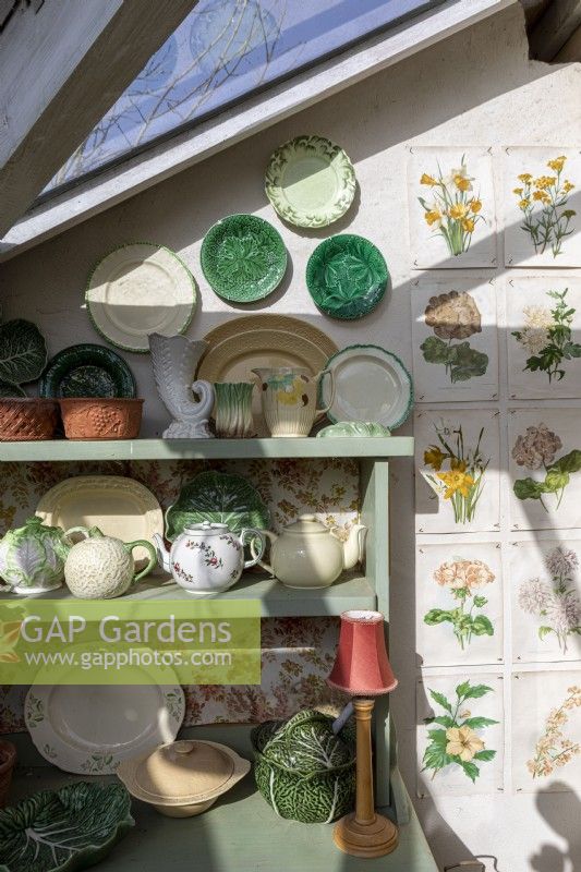 Interior of conservatory with dresser covered in antique crockery and gardening prints on wall
