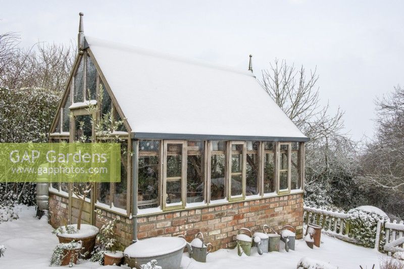 Gabriel Ash greenhouse in the snow with galvanised watering cans and containers