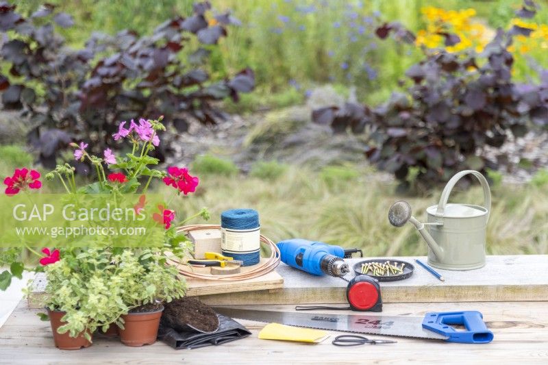 135cm X 22cm X 3.5cm Wooden board, saw, sandpaper, tape measure, screws, pencil, drill, copper wire, pliers/wire cutters, blue twine, watering can, compost scoop, plastic liner, snips, pelargoniums laid out on table