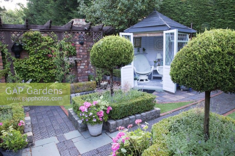 Secluded parterre garden with summerhouse. Paths and walls made of reclaimed cobbles and station platform tiles. Planted with Buxus sempervirens hedges infilled with Lavandula angustifolia, and Thuja standards