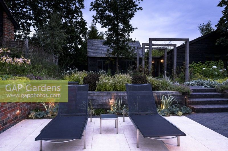 Contemporary garden in dusk with lights inset into steps and brick retaining wall in July. 