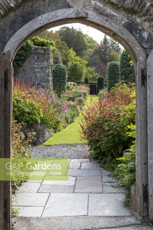 Looking through arched doorway down long borders in late summer garden