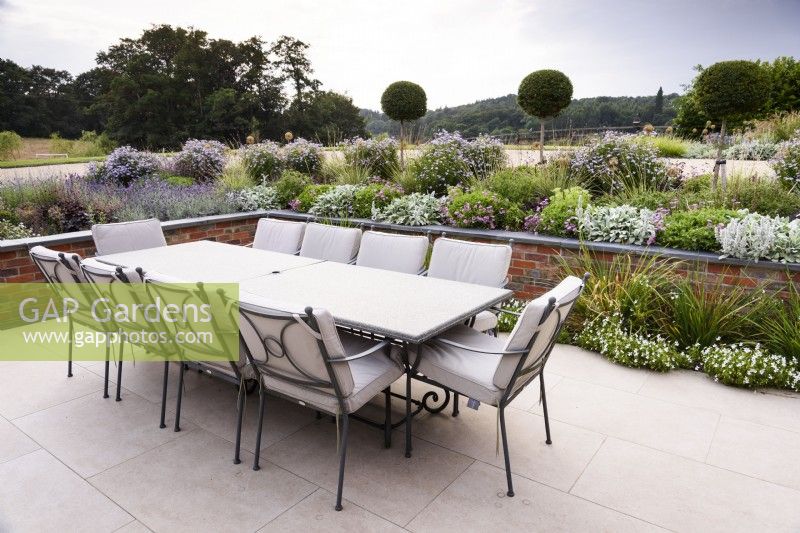 Dining area in a contemporary garden in July framed by a raised border featuring lollipop Ligustrum jonandrum in July