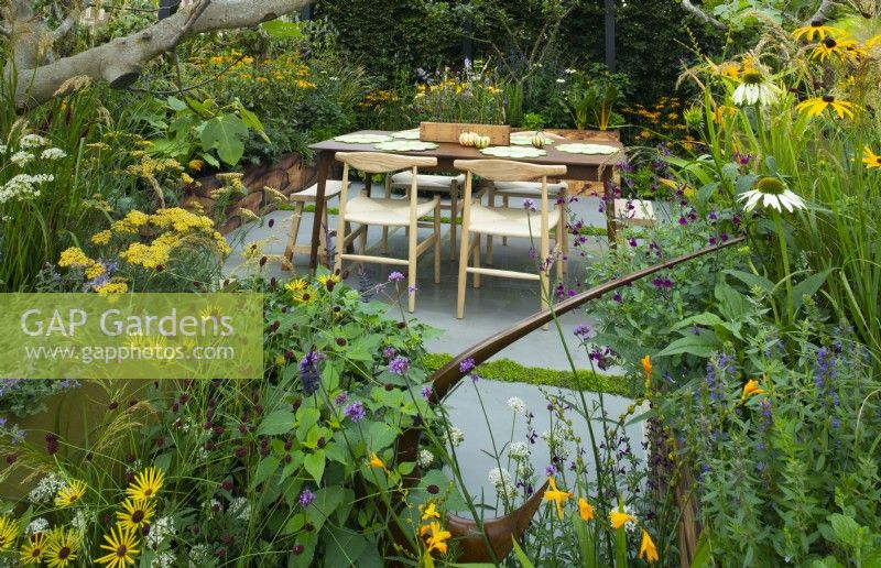 A dining area on a paved terrace surrounded by autumn planting set in wooden containers in the Parsley Box Garden, an edible sanctuary garden.