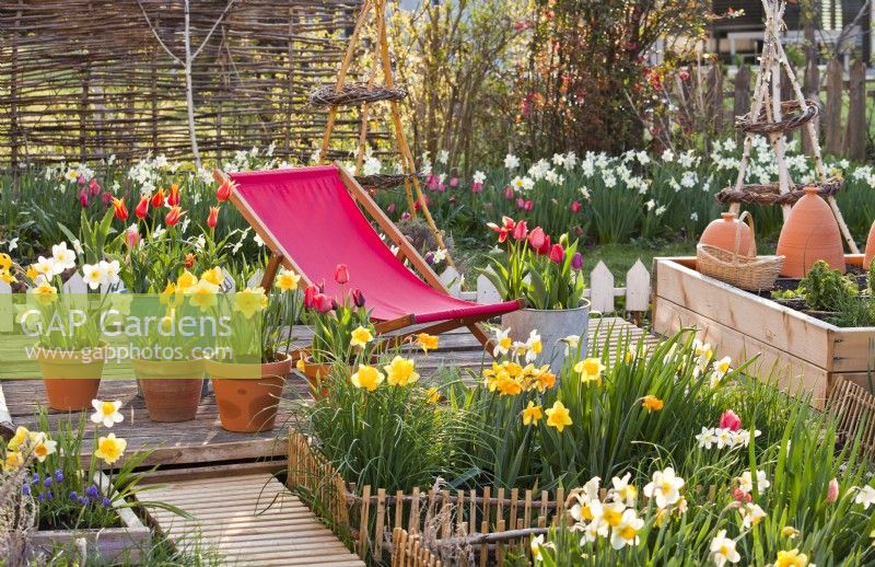 Deck chair on patio with spring containers and raised vegetable bed.