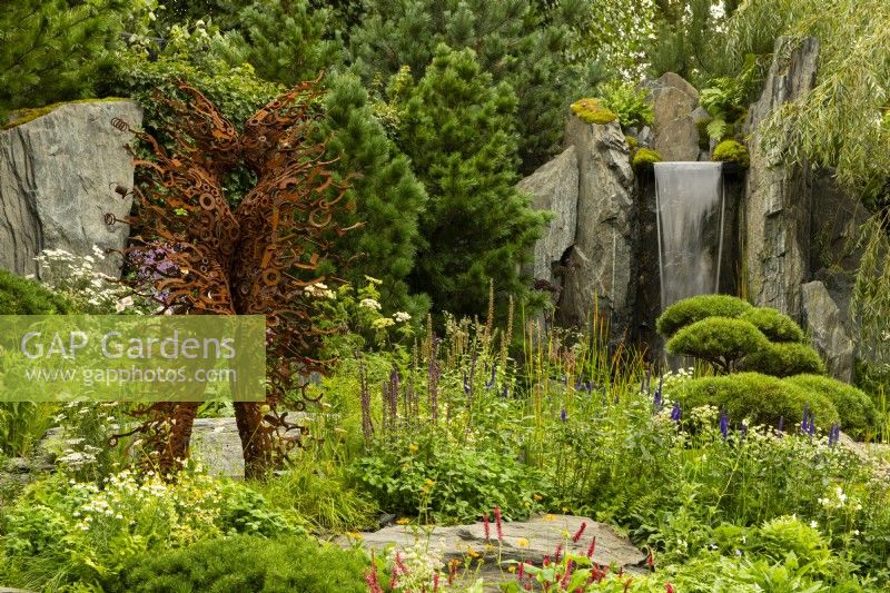 60 Degrees East, a garden between continents, a figurative metal sculpture beside a waterfall on a hillside surrounded by European and Asian planting.  Sculptures by Penny Hardy