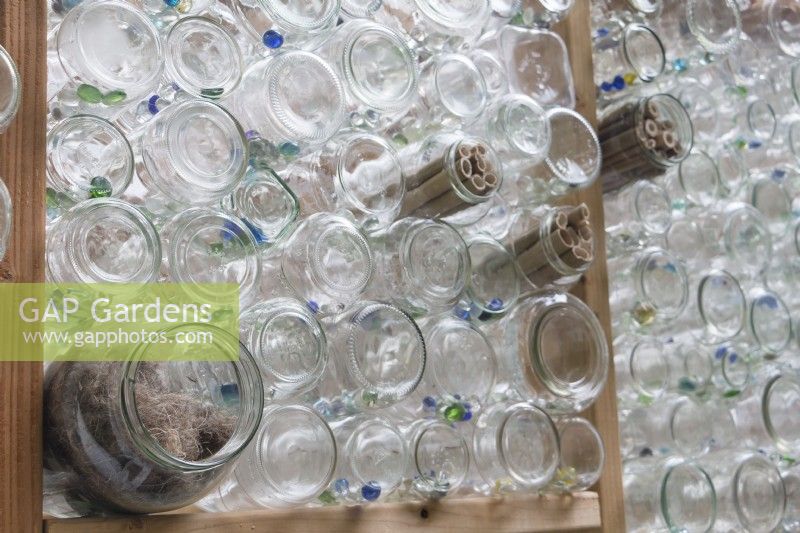 Nesting materials for birds are tucked into outward facing glass jars in recycled greenhouse walls