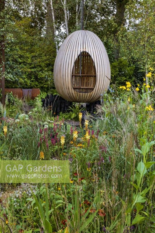 Yeo Valley Organic Garden. Naturalistic perennial meadow with pathway to focal point of steam-bent oak egg seat. Foreground planting includes Kniphofia
'Tawny King', Rudbeckia laciniata
'Herbstonne', Calamagrostis Ã—
acutiflora 'Karl Foerster', Calamagrostis
brachytricha, and various Persicarias.