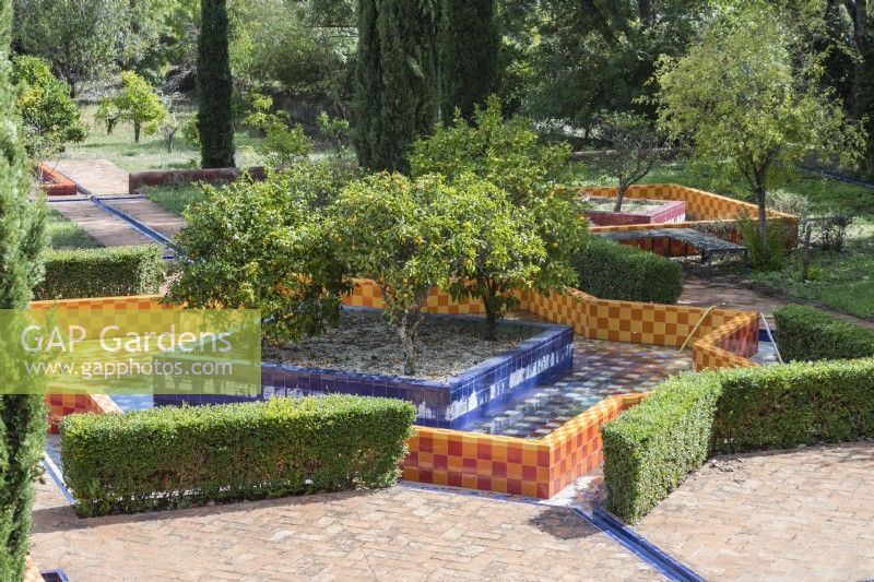 The citrus orchard in the lower garden with fruit trees in square raised beds surrounded by geometric shaped pool. Walls and pool faced with brightly coloured glazed tiles. Lisbon, Portugal, September.