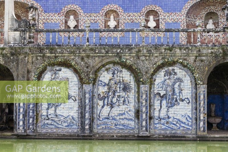 View across the Basin of the Knights pool to The Kings Gallery. Raised walkway with stone balustrade and niches containing busts of the Kings of Portugal. Walls above pond decorated with full sized representations made of glazed tiles or Azulejos of  Knights on horseback.  Lisbon, Portugal, September.